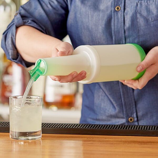 A person using a Choice white plastic pour bottle with green spout to pour a drink into a glass.