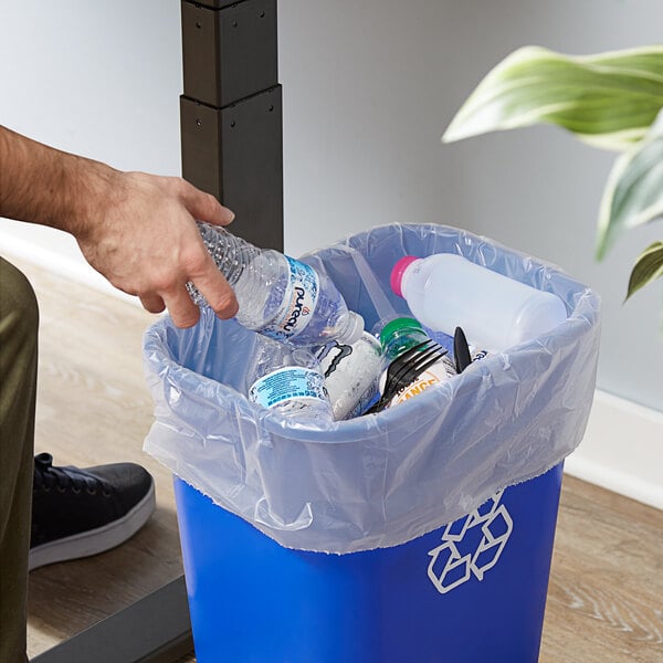 A hand putting a plastic bottle in a Lavex trash bag.