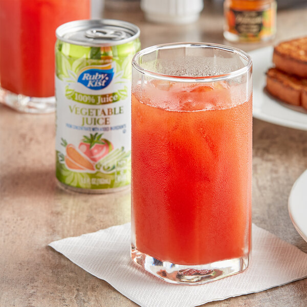 A glass of Ruby Kist vegetable juice next to a Ruby Kist juice bottle and a can of Ruby Kist vegetable juice.
