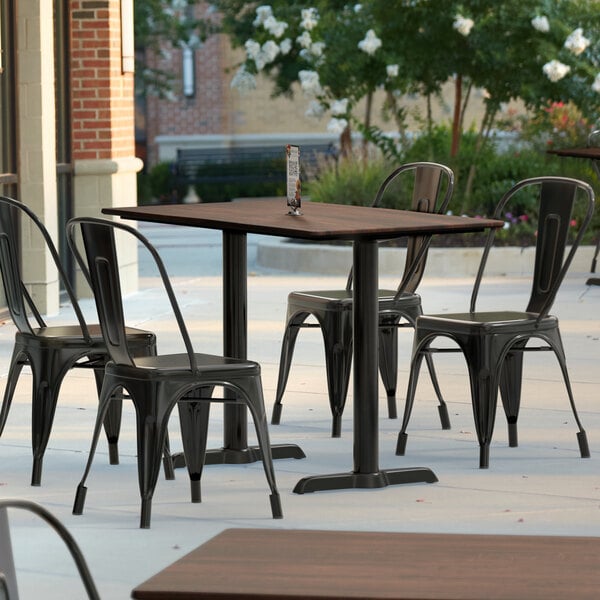 A Lancaster Table & Seating rectangular dining table with a textured walnut surface and outdoor base plates on a patio with chairs.