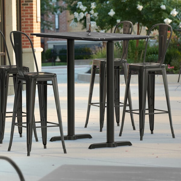 A Lancaster Table & Seating bar height table with a smooth finish and two black outdoor base plates on a patio.