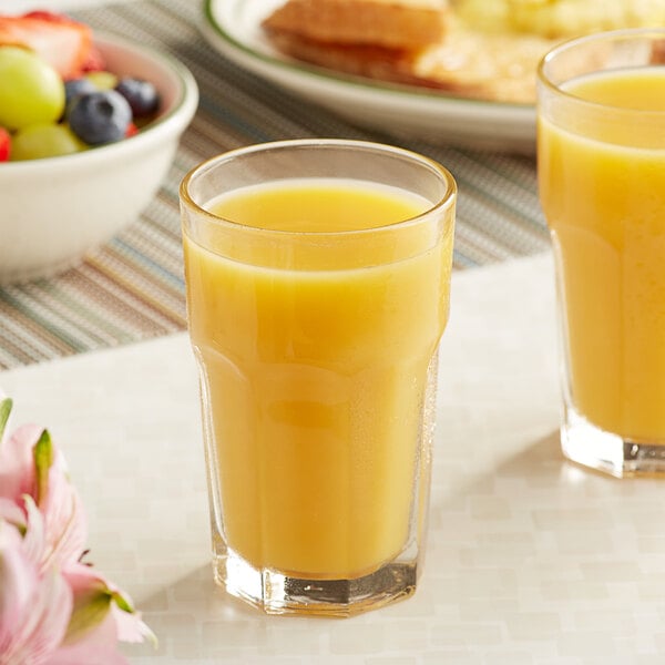 Two glasses of Ruby Kist orange juice next to a bowl of fruit.