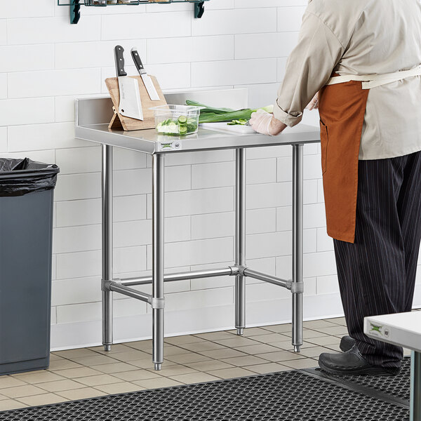 A man in an apron standing at a Regency stainless steel work table.