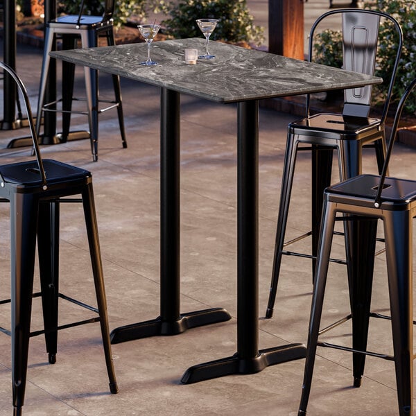 A rectangular bar height table with a smooth dark finish and two sturdy black base plates, designed for outdoor use.