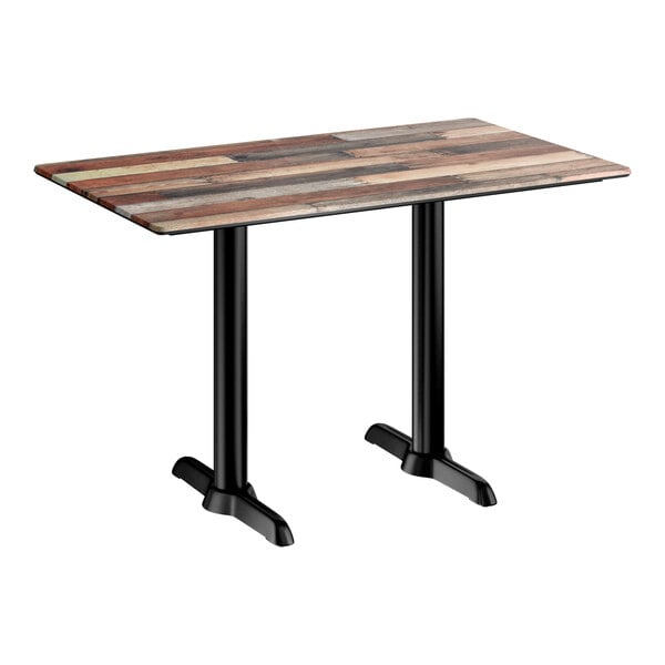 A rectangular standard height table with a textured mixed plank finish top and two black end outdoor base plates.