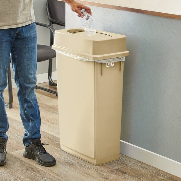 A man standing next to a Lavex beige slim rectangular trash can with a plastic liner.