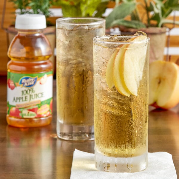 A glass of Ruby Kist apple juice and a bottle of Ruby Kist apple juice on a table.