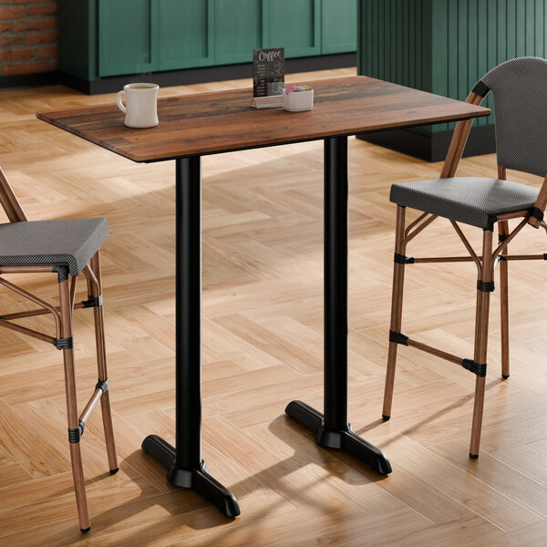 A rectangular bar height table with a textured farmhouse finish and two black metal base plates.