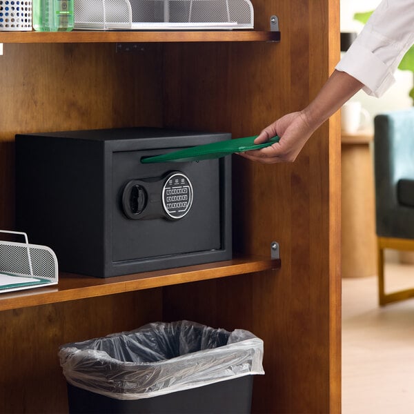 A black steel depository safe with an electronic keypad lock placed on a wooden shelf.