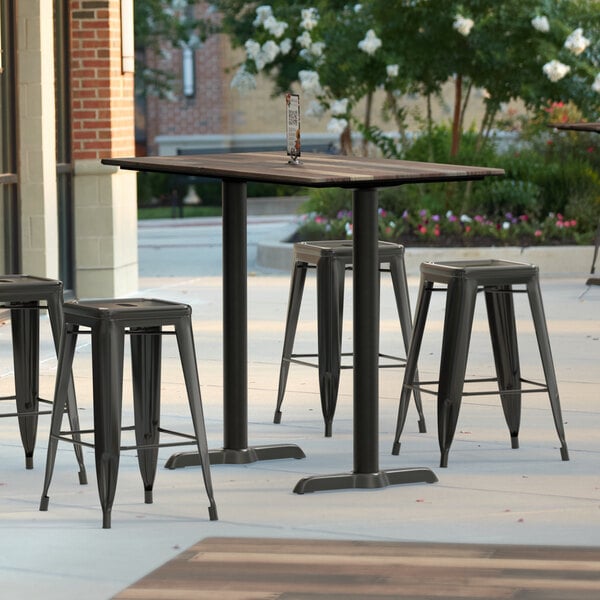 A Lancaster Table & Seating rectangular counter height table with textured mixed plank finish and two outdoor base plates on a patio.