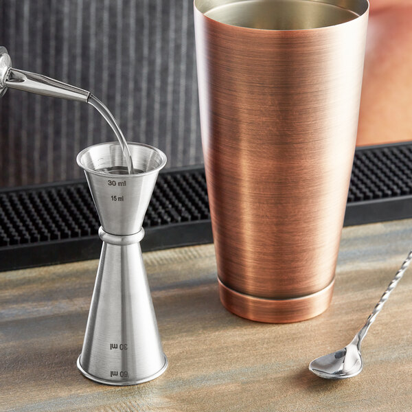 A Tablecraft stainless steel Japanese jigger with a metal cup and spoon.