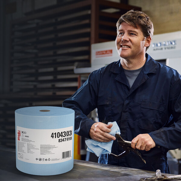 A man in a blue shirt and blue pants smiling while holding a large roll of blue WypAll X80 wipers.
