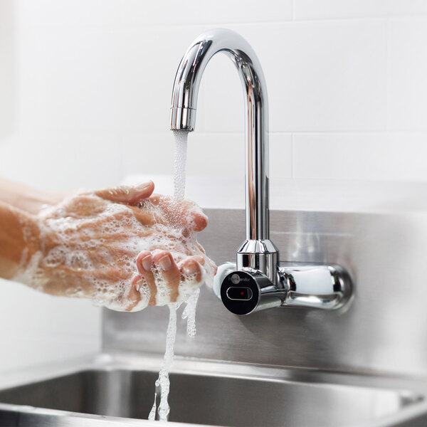 A person using the InSinkErator warm handwash system to wash their hands under a faucet on a metal counter.