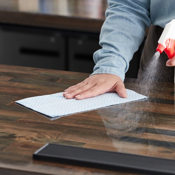 A person cleaning a counter in a professional kitchen with a blue WypAll foodservice wiper.