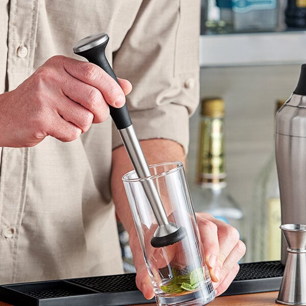 A person holding a OXO stainless steel muddler in a glass.