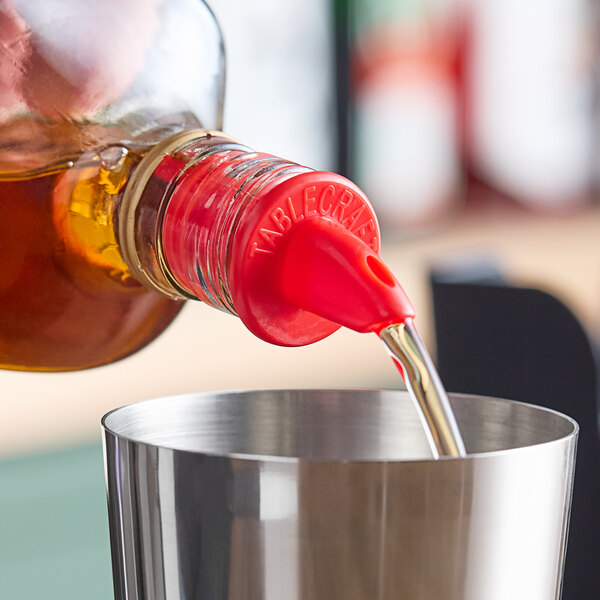 A person using a TableCraft red plastic liquor pourer to pour a bottle of liquid into a cup.