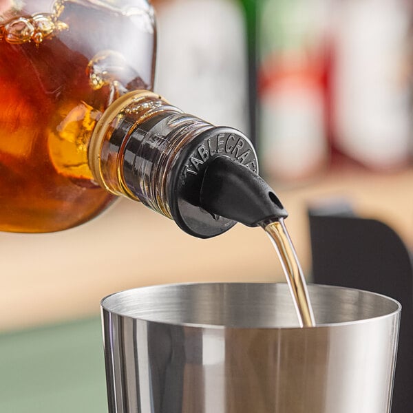 A person using a TableCraft black liquor pourer to pour alcohol into a cup.
