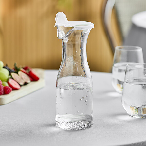 A clear polycarbonate decanter filled with water on a table with glasses