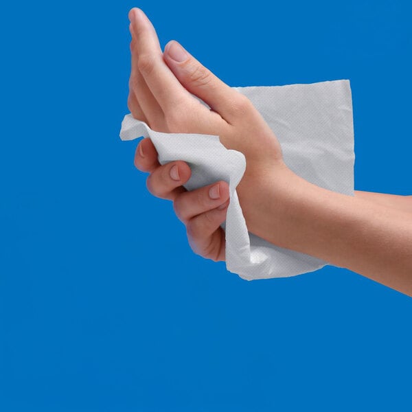 A hand is wiping another hand with a white paper towel against a blue background.