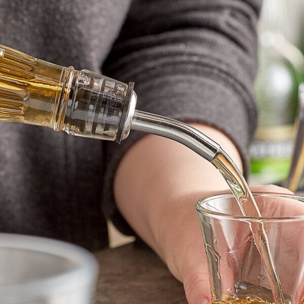 A person using a TableCraft chrome-plated liquor pourer to pour whiskey into a glass on a counter.