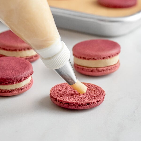 A pastry bag being used to decorate pink and white macaroons.