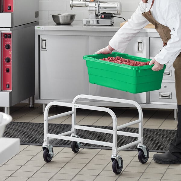A man in a kitchen holding a Regency green meat lug rack with a green meat lug full of food.