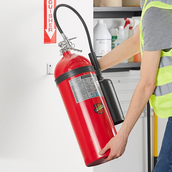 A man in a yellow vest holding a Buckeye carbon dioxide fire extinguisher.