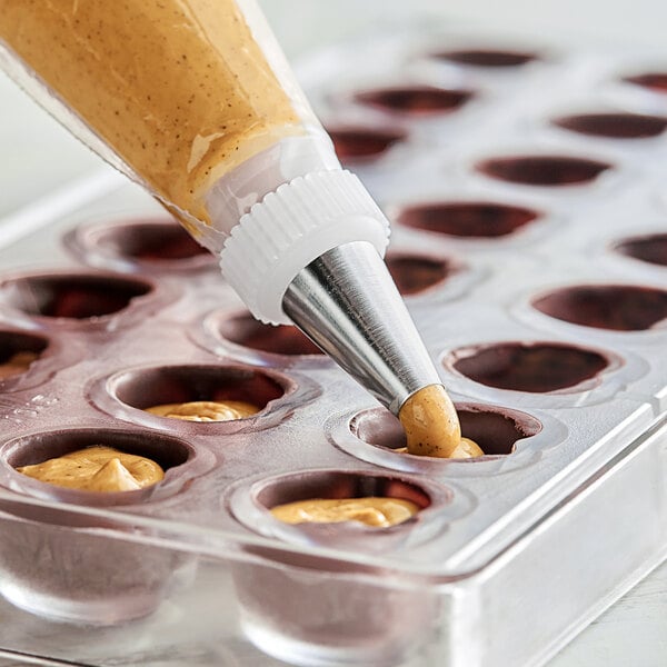 A pastry bag being used to fill chocolates with American Almond Praline/Hazelnut Paste.