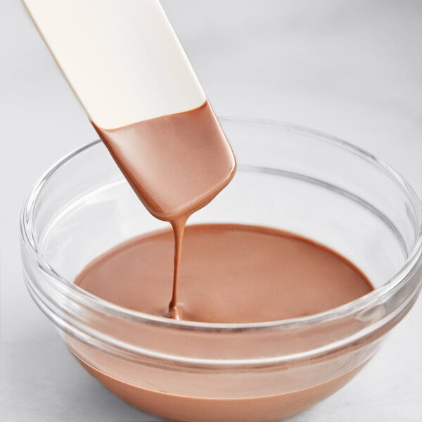 A spoon pouring Cacao Barry Blonde Pate a Glacer into a bowl of liquid.