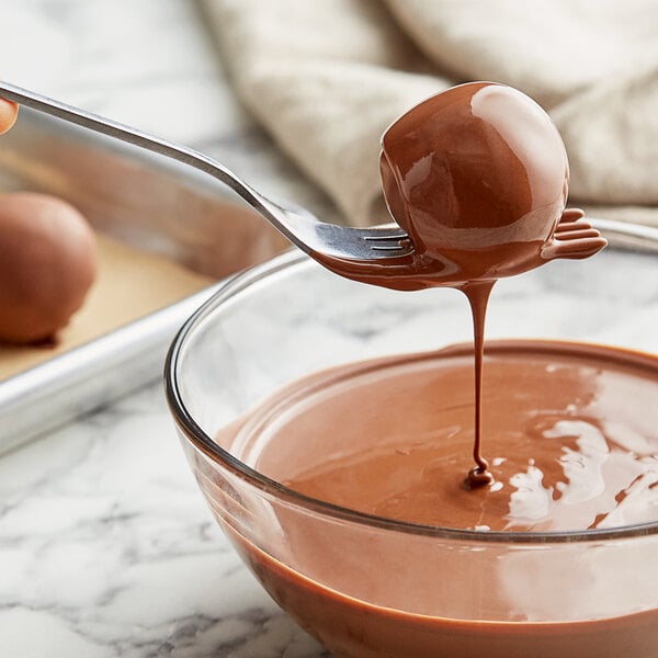 A spoon pouring Cacao Barry Blonde Pate a Glacer into a bowl of liquid.