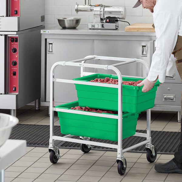 A man in a chef's uniform pushing a green Regency lug rack with meat inside.