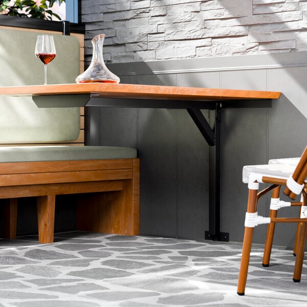 A black metal cantilever table base supporting a wooden tabletop in a restaurant booth setting.
