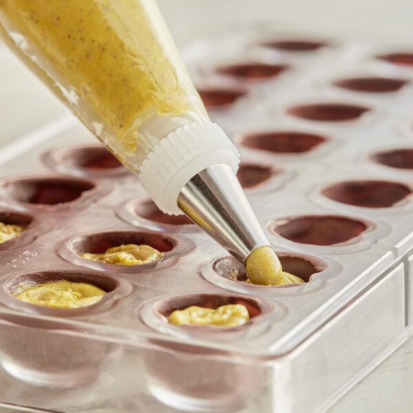 A plastic container of American Almond Pistachio Paste with a pastry bag of the paste on a baking tray.