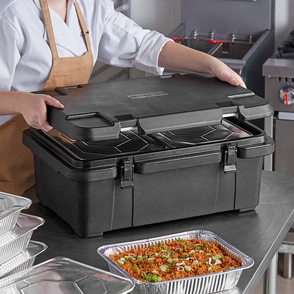 A person in a brown apron using a CaterGator black food pan carrier to hold a tray of food with rice and green onions.