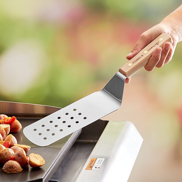 A hand using a Dexter-Russell perforated turner to flip vegetables on a grill.