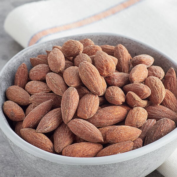 A white bowl filled with roasted salted almonds on a table.