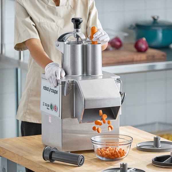 A woman using a Robot Coupe CL50 Ultra food processor to dice carrots.