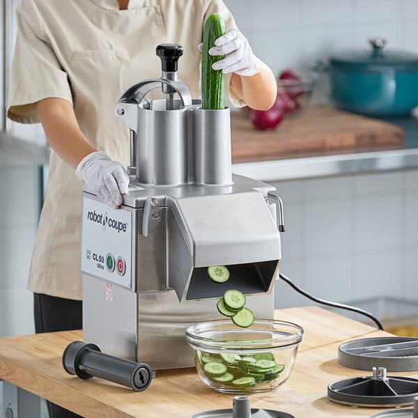 A woman using a Robot Coupe commercial food processor to slice cucumbers.