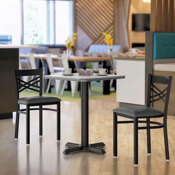 A square reversible table with a white and gray slate laminated top, set in a dining area with two black chairs.