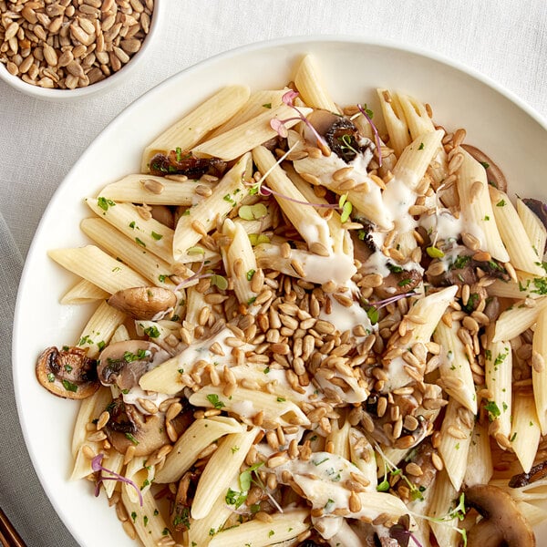 A white plate with pasta, mushrooms, and sunflower seeds.