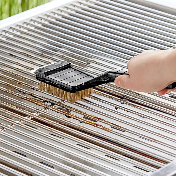 A hand holding a Quickie grill brush over a grill.