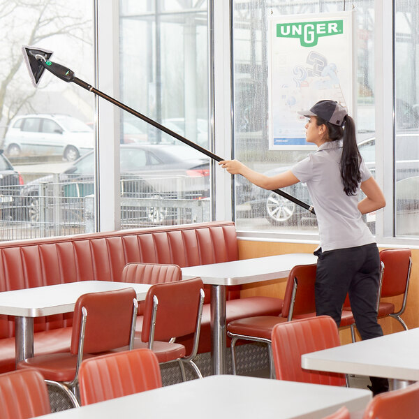 A woman using an Unger Stingray microfiber cleaning stick to clean a table in a restaurant.
