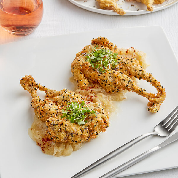 A plate with a Manchester Farms quail and utensils.