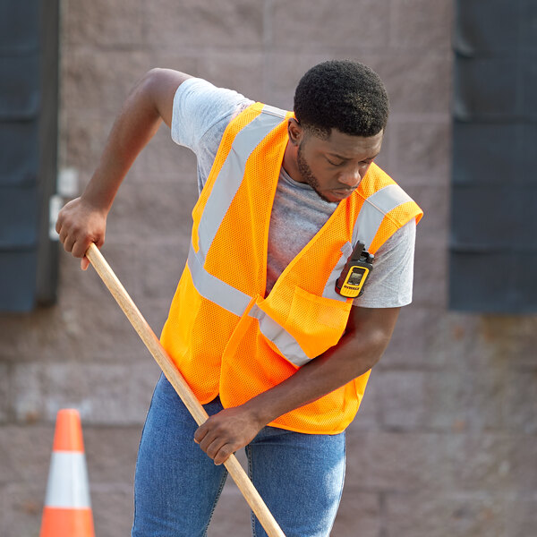 A man in an Ergodyne orange reflective mesh vest using a shovel.