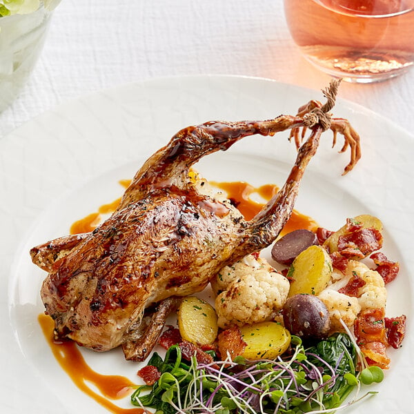 A white plate topped with a Manchester Farms whole quail and vegetables on a table.