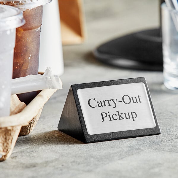 An American Metalcraft "Carry-Out / Pickup" sign on a table with a cup of coffee and a take out menu.