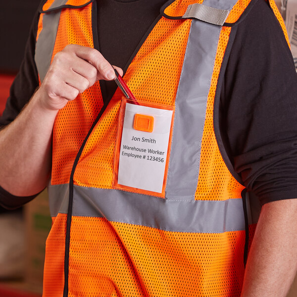 A person wearing an orange Ergodyne high visibility vest with ID holder holding a clipboard.