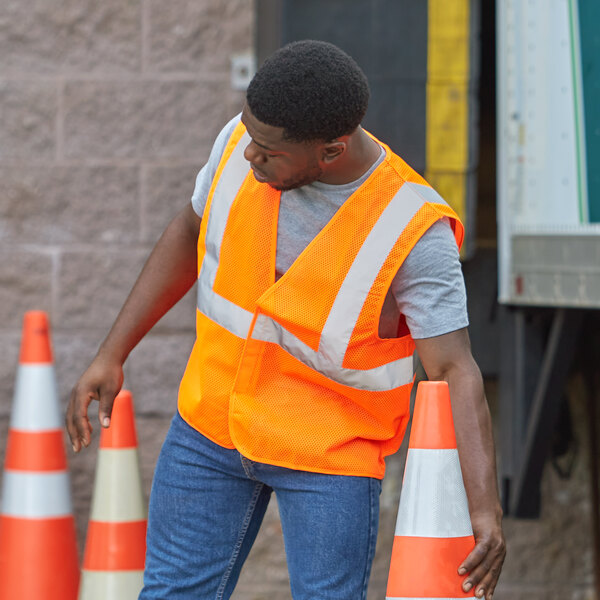 A man in a Ergodyne orange reflective vest standing next to orange cones.