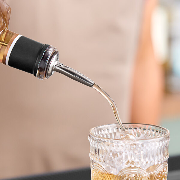 A bartender using an American Metalcraft stainless steel liquor pourer to pour liquid into a glass on a counter.