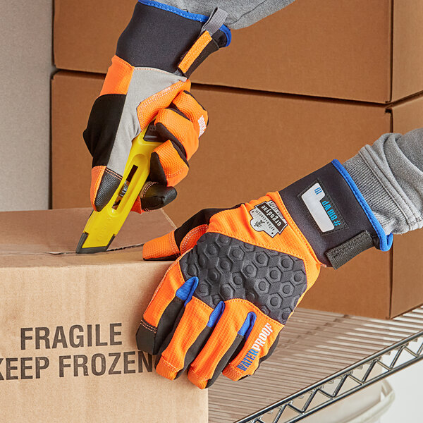 A person wearing Ergodyne ProFlex orange thermal waterproof work gloves cuts a box.